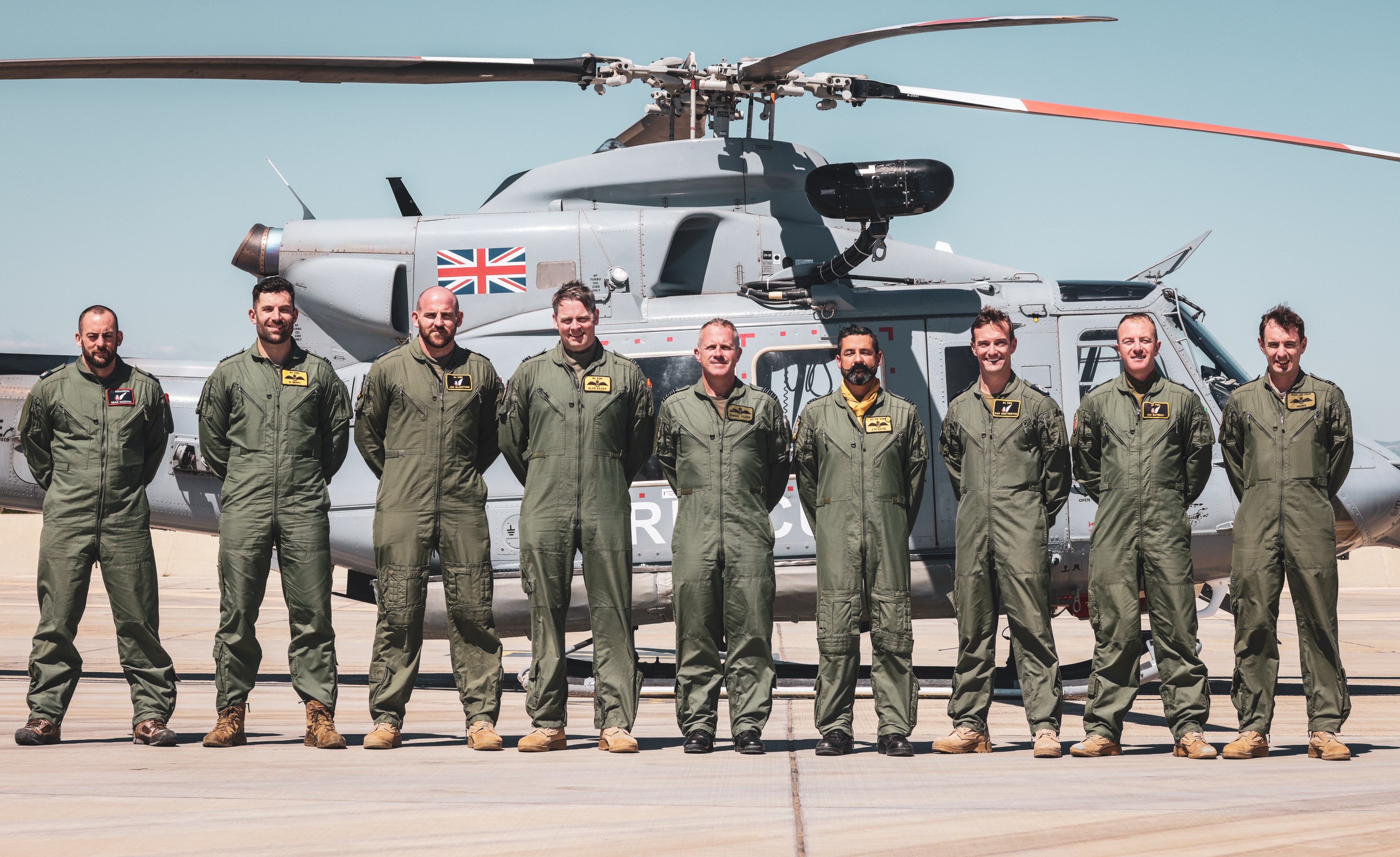 Image shows RAF pilot squadron standing by their helicopter.